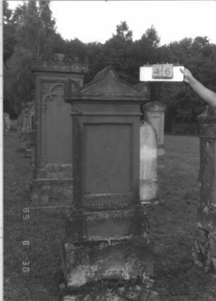 Grabstein 46 (Index: 99609682) Material: Sandstein Zustand: verwittert, Schriftplatte fehlt Maße HxBxT: 190x65x30 cm Beschreibung: Stele, Abdeckplatte mit Giebelaufsatz, Seitenakrotere, rechteckige Schriftplatte fehlt, getreppter Sockel: Grabstein 46