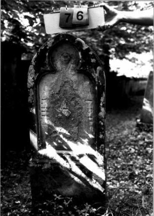 Grabstein 76 (Index: 100109329) Material: Sandstein Zustand: völlig verwittert, nur einzelne Buchstaben erkennbar Maße HxBxT: 117x49x12 cm Beschreibung: Stele, Sockel, Spitzbogenabschluß, Schriftfeld mit Maßwerk: Grabstein 41904