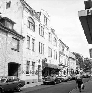 Bahnhofstraße: parkende Pkw und Passanten, rechts das Café Arnold und weitere Wohn- und Geschäftsgebäude