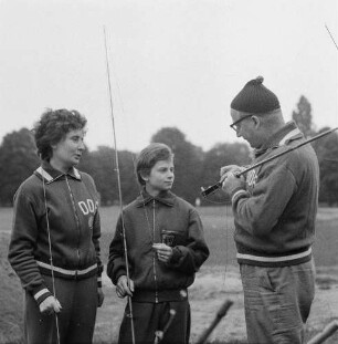 Helga Wischer-Rudolph und ihr Trainer Horst E. Rudolph im Gespräch mit einer Jugendlichen beim Sportangeltraining auf einem Fußballplatz