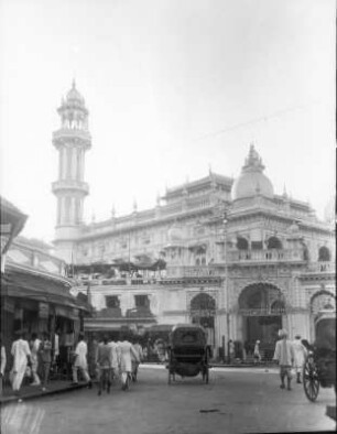 Bombay. Straße mit Passanten und Kutschen gegen Große Moschee