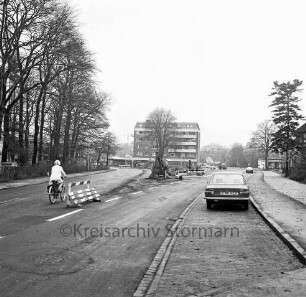 Möllner Landstraße: vorn neue Straßenführung: links alte Straßenführung mit Fahrradfahrerin: dazwischen Absperrung und Bauarbeiten: vorn rechts parkender Pkw: hinten Mitte Wohn- und Geschäftsblock: links Baumreihe