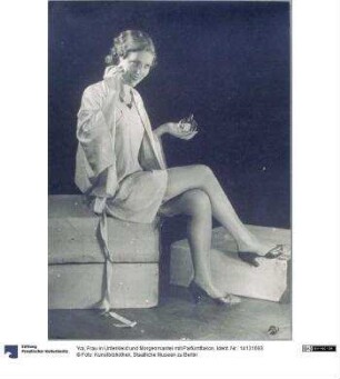 Frau in Unterkleid und Morgenmantel mit Parfümflakon