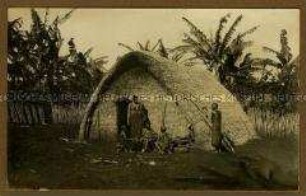 Afrikanische Frau mit Kindern an der Giebelseite einer Hütte