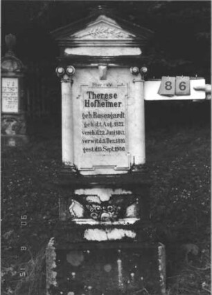 Grabstein 86 (Index: 100106485) Material: Marmor, Sockel Sandstein Zustand: gut, verwittert, Mittelaufsatz fehlt Maße HxBxT: 168x58x23 cm Beschreibung: ädikulaartige Stele mit Giebeldach, Mittelaufsatz fehlt, ionische 3/4-Säulen, getreppter Sockel Symbolik: Blumengebinde, Palmzweig: Grabstein 86
