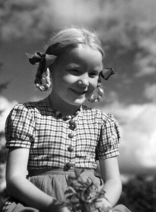 Kinderbilder. Porträt eines kleinen Mädchens mit Affenschaukelfrisur, auf einem Koppelzaun sitzend