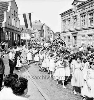 Kindervogelschießen: Umzug: Lübecker Straße: Mädchen mit Blumenbögen, dahinter Blumenkrone: an den Straßenrändern Zuschauer: an Fassaden Fahnenschmuck, 4. Juli 1957