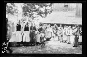 Festlich gekleidete Einheimische (vor allem Frauen) neben einem Kirchengebäude aus Holz