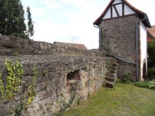 Kirchhof im Norden-Torhaus von Westsüdwesten (Romanisch) sowie im Westen anschließender Kirchhofmauer mit Treppe zum Wehrgang und erhaltenen Schießscharten in Brusthöhe