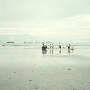 Accra. Surfboats : Accra (Ghana). Fischer mit Surfboat und Netz am Strand. Im Hintergrund auf Reede Frachtschiffe, 29. März 1959
