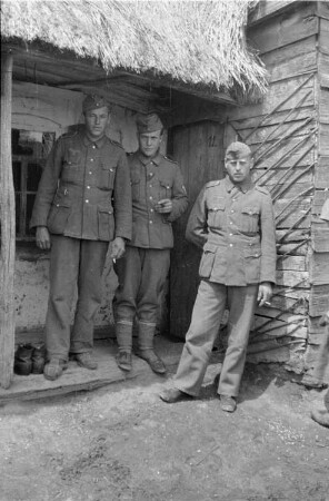 Zweiter Weltkrieg. Zur Einquartierung. Sowjetunion. Drei Angehörige der deutschen Wehrmacht vor einer Bauernhütte