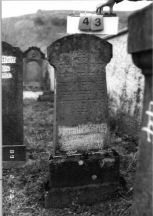 Grabstein 43 (Index: 99798324) Material: Sandstein Zustand: leicht verwittert Maße HxBxT: 121x35x17 cm Beschreibung: Stele mit überkragendem Segmentbogenabschluß, Sockel Besonderheit: Kindergrab: Grabstein 43