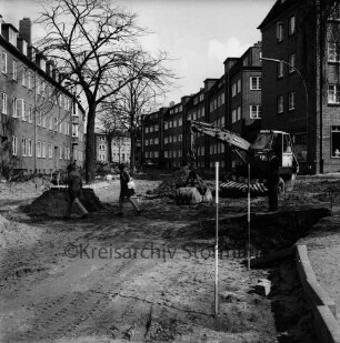 Mewesstraße: Blick Richtung Ratzeburger Straße: rechts Einmündung der Reimer-Hansen-Straße mit Bagger: links zwei Fußgänger in Baustelle: dahinter Bäume: hinten Wohnblocks