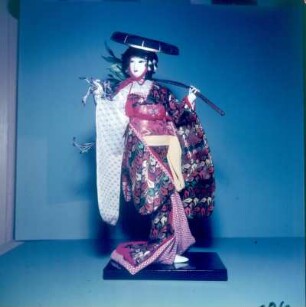 Japan. Japanische Puppe. Fuji Musume (Glyzinen-Mädchen) darstellend, mit schwarz lackiertem Bambushut und einem Glyzinenzweig