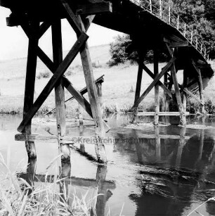 Klein Barnitz: Trave: Holzbrücke für Fußgänger mit Schäden an den Jochen: hinten Wiese und Bäume
