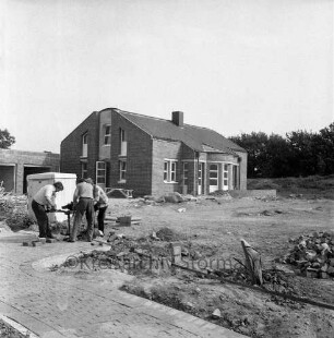 Bargteheide: Kreisgymnasium II [später Gymnasium Eckhorst]: Eckhorst: vor Fertigstellung: Arbeiter beim Herrichten der Außenanlagen: Weg, Haufen mit Pflastersteinen: hinten Nebengebäude, Garagen