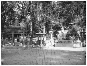 Nara. Heilige Laternen an kleinem Schrein mit Torii neben Skulptur eines heiligen Hirschen im Nara-Park