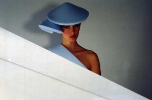 Model in Schaumstoffmode : Model mit hellblauem Schaumstoffhut hinter einem Neonleuchtkörper