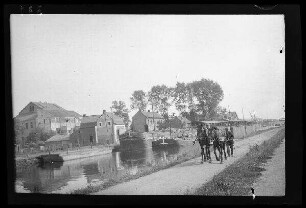 Courrières (?) (Dep. Pas-de-Calais, Frankreich): 2 Kähne in einem Kanal, im Hintergrund Gebäude, im Vordergrund ein Mann hinter einem Pferdegespann (Distanzaufnahme)