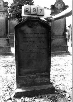 Grabstein 297 (Index: 99797840) Material: Sandstein, weiß Zustand: stark verwittert Maße HxBxT: 94x49x10 cm Beschreibung: Stele, giebelartiger oben abgeflachter Abschluß, Sockel Symbolik: Rose: Grabstein 297
