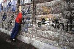 Mann guckt durch Spalt in der Berliner Mauer