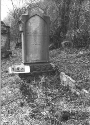 Grabstein 143 (Index: 99608827) Material: Sandstein Zustand: beschädigt mit kleinem Textverlust Maße HxBxT: 131x58x22 cm Beschreibung: Stele, getreppter Rustikasockel, getreppter giebelaritger Abschluß, Schriftfeld eingetieft mit Spitzbogenabschluß: Grabstein 143