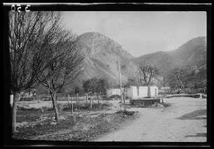 [Rucãr (?) (Rumänien)]: unbefestigte Ortsstraße, dahinter eine Gebäuderuine, im Hintergrund ein Bergmassiv