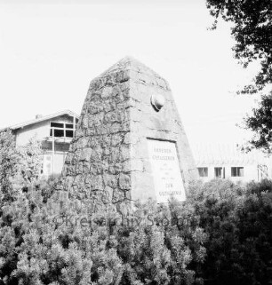 Dorfstraße: Ehrenmal: vorn Tannen: rechts oben Baumäste: hinten Häuser