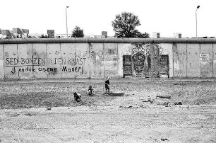 Spielende Kinder an der Berliner Mauer mit Inschrift "SED-Bonzen in den Knast - an die eigene Mauer"