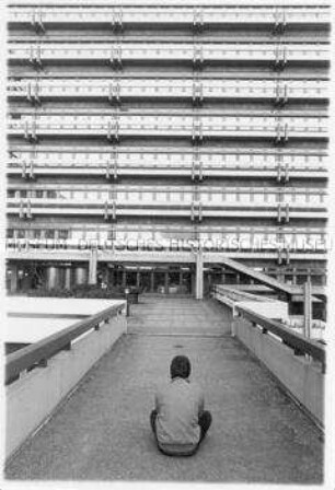 Junger Mann sitzt vor einem Hochhaus (Altersgruppe 18-21)