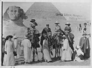 Gizeh (Ägypten). Touristen und einheimische Führer mit Kamelen vor der Sphinx und den Pyramiden von Gizeh