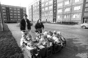Kinderkrippenwagen Neubau Süd : Zwei Kinderkrippen Erzieherinnen fahren die Gruppenkinder in Krippenwagen durch ein Plattenbau-Wohngebiet