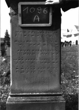 Grabstein 1096 (Index: 100104155) Material: Sandstein Zustand: im oberen und unteren Bereich stark verwittert, sonst noch gut erhalten Maße HxBxT: 138x49x25 cm Beschreibung: Stele auf getrepptem Sockel, auskragender Aufsatz mit Voluten, Mohnkapseln und -blättern Symbolik: Mohnkapseln/-blätter, Voluten: Grabstein 1096A