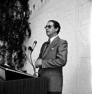 Schell Baumarkt: Industriestraße: Einweihung: Innenaufnahme: Baustoffhalle: Geschäftsführer Jörn-Peter Schell hält Rede, am Rednerpult mit Mikrofon: Grünpflanze, Wimpelgirlande, 28. August 1975