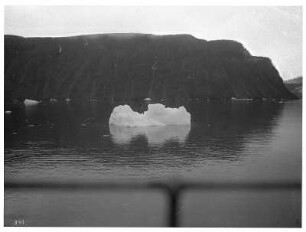 Spitzbergen. Schwimmender Eisberg gegen Felsenküste und Buchtlandschaft über die Reeling des Hochseepassagierdampfers "Victoria Luise"