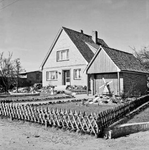 Neubausiedlung: Einfamilienhaus mit Garage: davor geschmückter Vorgarten mit Jägerzaun: links Baum: vorn rechts Modellwindmühle