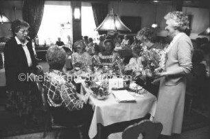Hausfrauenbund Reinfeld: Gasthof, Saal: Jahresversammlung: rechts stehend Vorsitzende Thea Basse mit Blumenbesteck: links Damen an gedeckten Tischen: 31. März 1989
