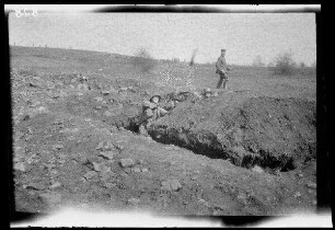 Übungsgelände I bei Mouzon (Dep. Ardennes, Frankreich): Soldat mit Stahlhelm beim Werfen einer Stilgranate aus einem Graben (Vorderansicht, Distanzaufnahme) ("im Graben")