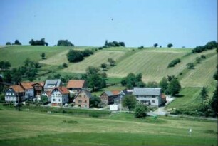 Blick über den Ort, dahinter Stufenraine mit Feldgehölzen, die die Hofbreiten nachzeichnen (Geländeflur)