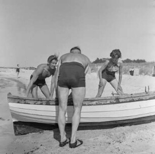 Drei Personen mit Ruderboot am Strand