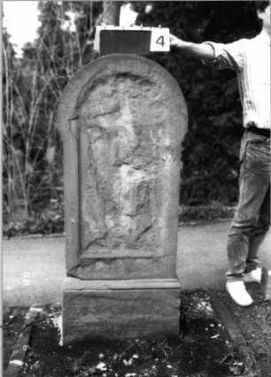 Grabstein 4 (Index: 99792878) Material: Sandstein Zustand: gänzlich verwittert Maße HxBxT: 138x58x30 cm Beschreibung: Stele, Sockel, überstehender Rundbogenabschluß, Schriftfeld eingetieft mit Rundbogenabschluß: Grabstein 4