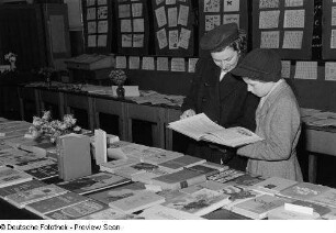 Ausstellungsbesucher an einem Bücherstand ein Buch lesend