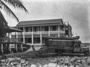 Blick auf eine Villa : Blick auf eine Villa, davor Person auf einer Mauer und Automobile