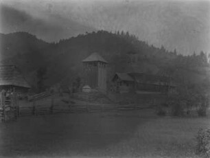 Holzkirche : Blick über ein Feld auf eine Holzkirche und den hölzernen Glockenturm.