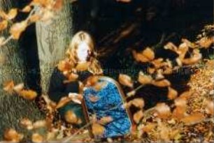 An einem Baum gelehnt sitzende junge Frau mit Spiegel (Altersgruppe 18-21)