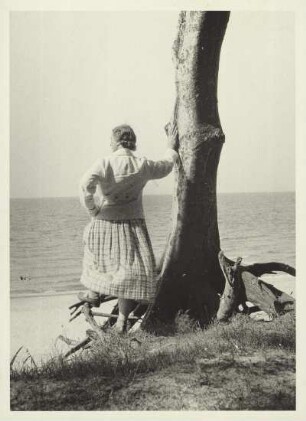 Kolberg (heute: Kolobrzeg / Polen). An der Ostseeküste. Eine Frau lehnt an einem Baumstamm und blickt aufs Meer