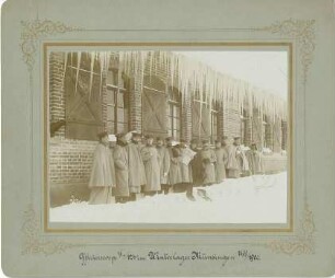 Offizierskorps (zwölf Soldaten) des II. Bataillons des Regiments im Winterlager Truppenübungsplatz Münsingen und eine Dame im Schnee vor Backsteingebäude