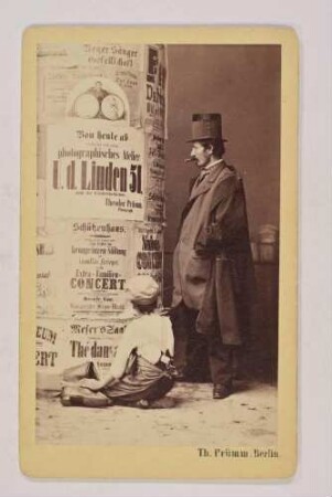 Mann und Junge vor einer Litfasssäule mit einer Anzeige anlässlich der Neueröffnung des Fotoateliers von Theodor Prümm