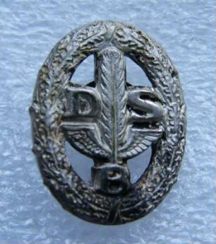 Leistungsabzeichen für Handelskammerprüflinge in Silber Deutscher Stenografenbund (mit Broschennadel) : Sammlung Beinhorn. Leistungsabzeichen für Handelskammerprüflinge in Silber Deutscher Stenografenbund (DSB mit geflügelter Feder im Eichenkranz, mit Broschennadel; rückseitig: Ges. Gesch.). Metall, versilbert; Maße 18 x 14 mm (1926/1933). Dresden: SLUB R c 0201