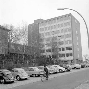 Erweiterungsbau "Hochhaus" vor Einweihung [später Gebäude B]: III. Bauabschnitt: links Hauptgebäude [später Gebäude A], dazwischen Verbindungstrakt: im Vordergrund Bangertstraße mit Parkplätzen für Pkw und Fahrradfahrer